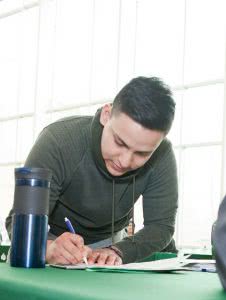 A male student is writing on a paper on the desk.